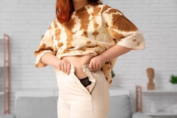 Image of woman trying to do her trousers up after pregnancy weight gain South Side